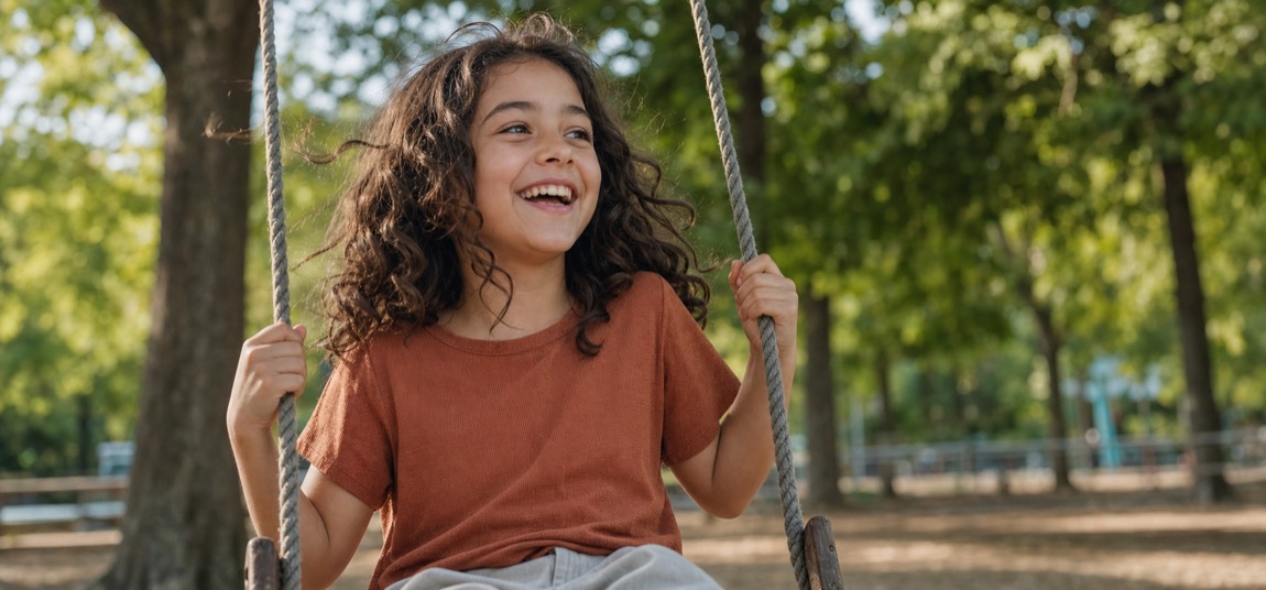 Niña riendo mientras se columpia en un parque